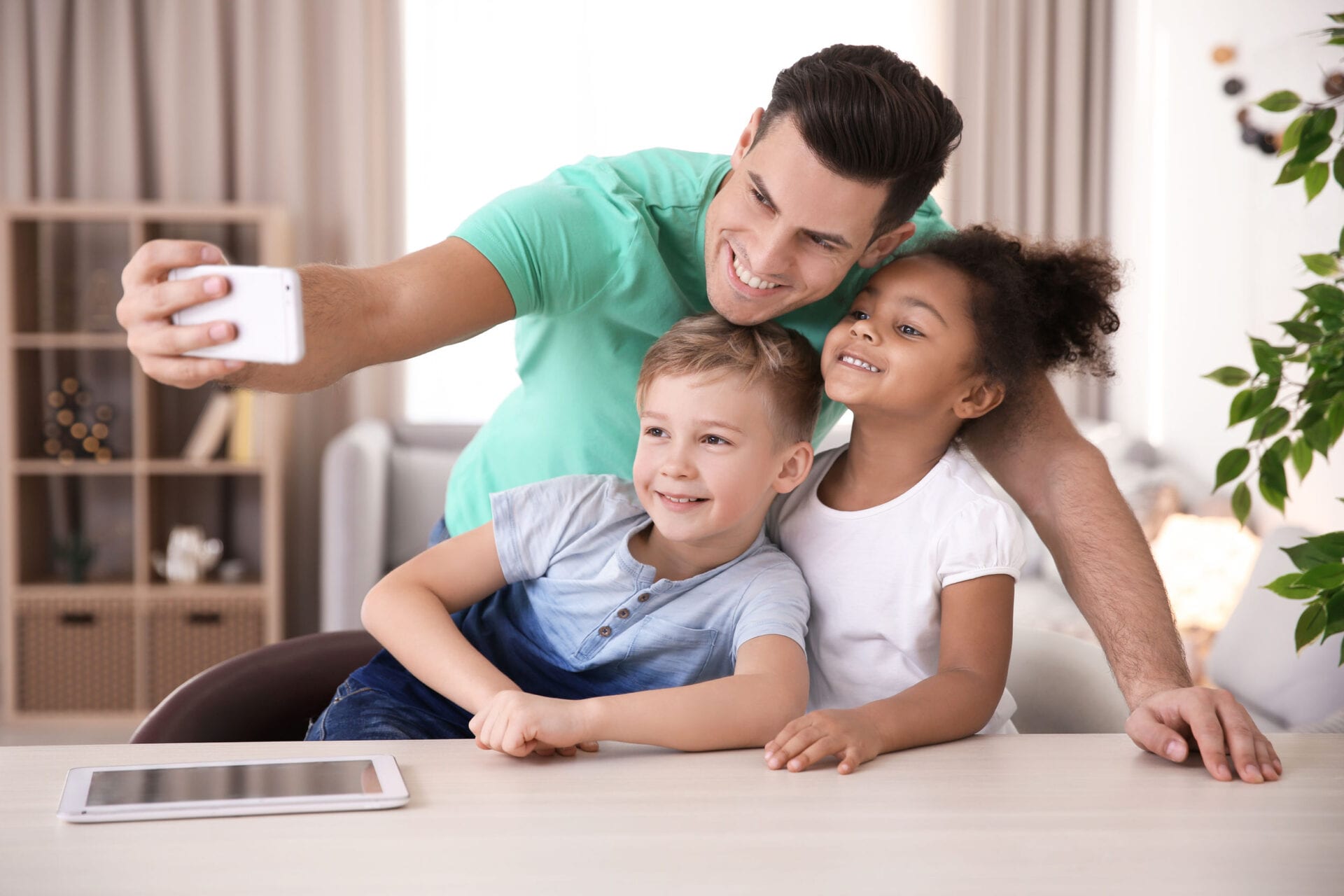 Young man taking selfie with little kids indoors. Child adoption